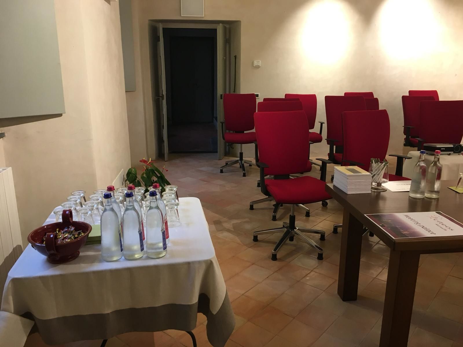 Une salle de conférence avec des chaises rouges, une table sur laquelle sont posées des bouteilles d’eau et un bol de collations, et une porte visible au fond.