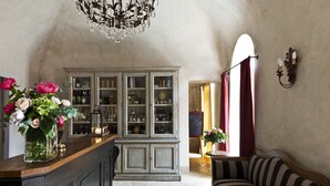 A room with a wooden bar, a striped sofa, a cabinet with glass doors, and a chandelier. - Relais Del Maro (Borgomaro)