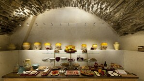 A stone-walled room with a buffet table displaying various food items and kitchenware. - Relais Del Maro (Borgomaro)
