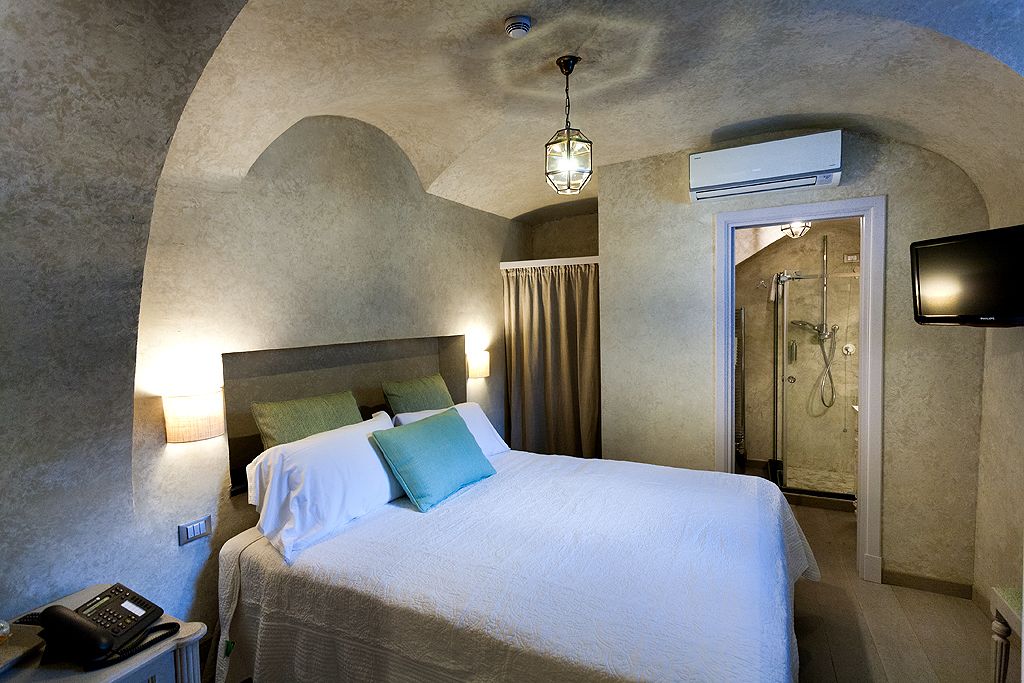 A hotel room with a bed, a telephone, an air conditioning unit, a television, and a shower area.