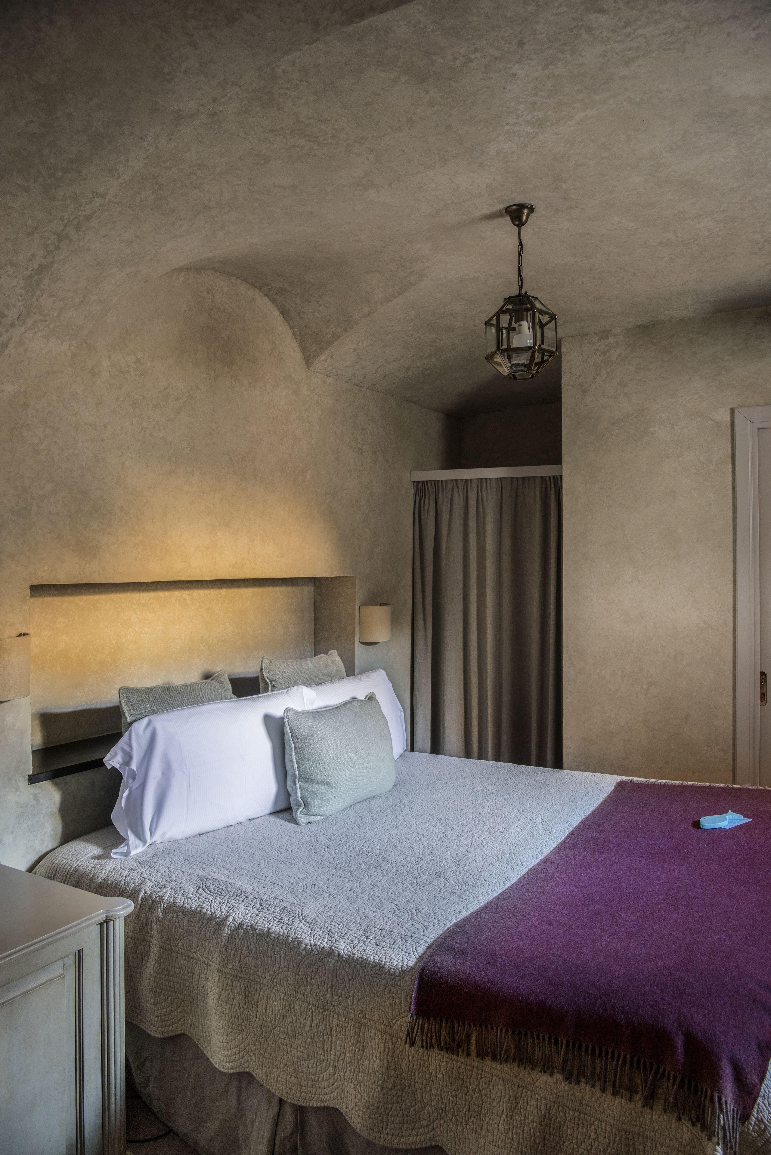 Un dormitorio con cama, cabecero, mesita de noche, lámpara y lámpara colgante.