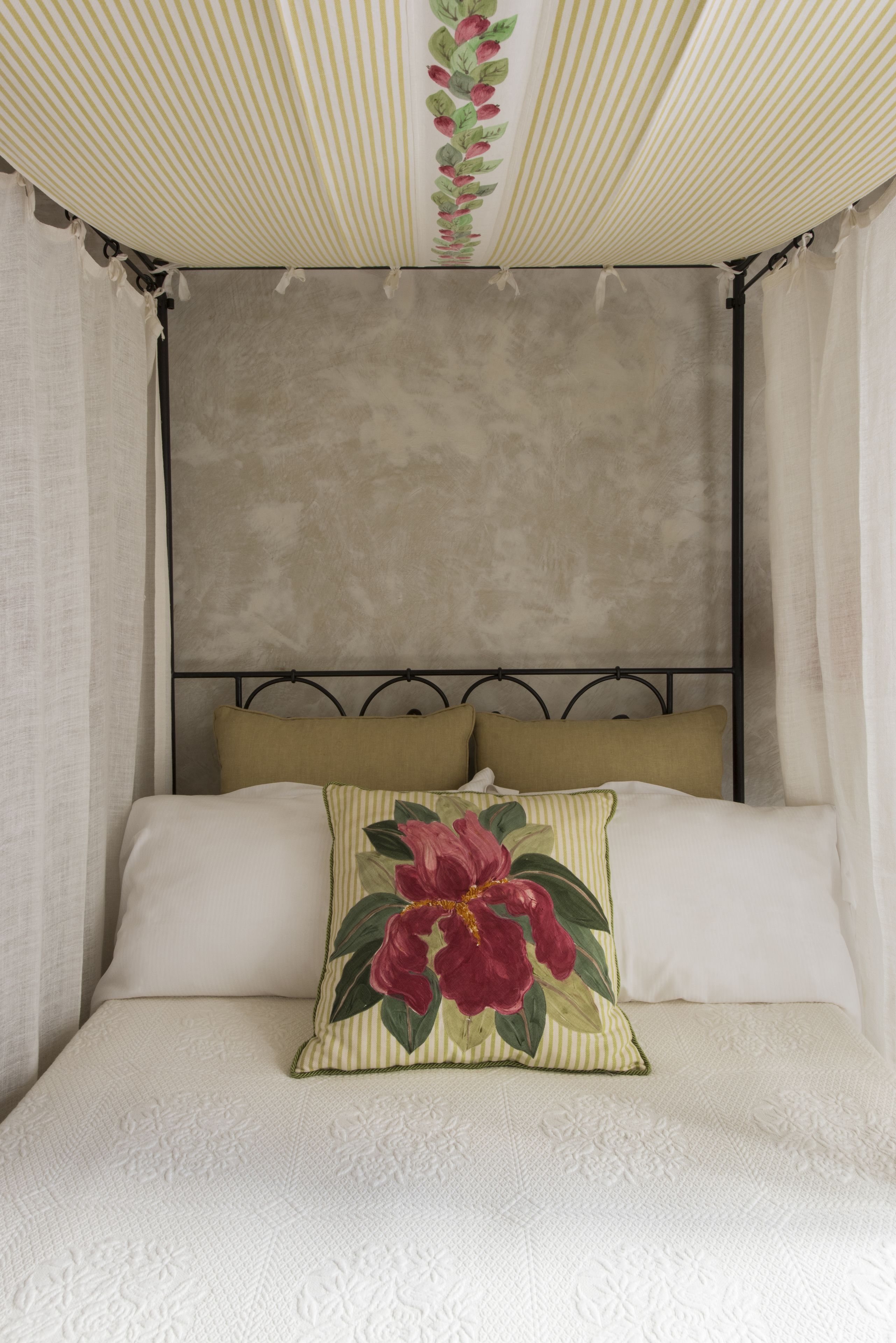 Un letto con baldacchino, poggiatesta e cuscino decorativo.