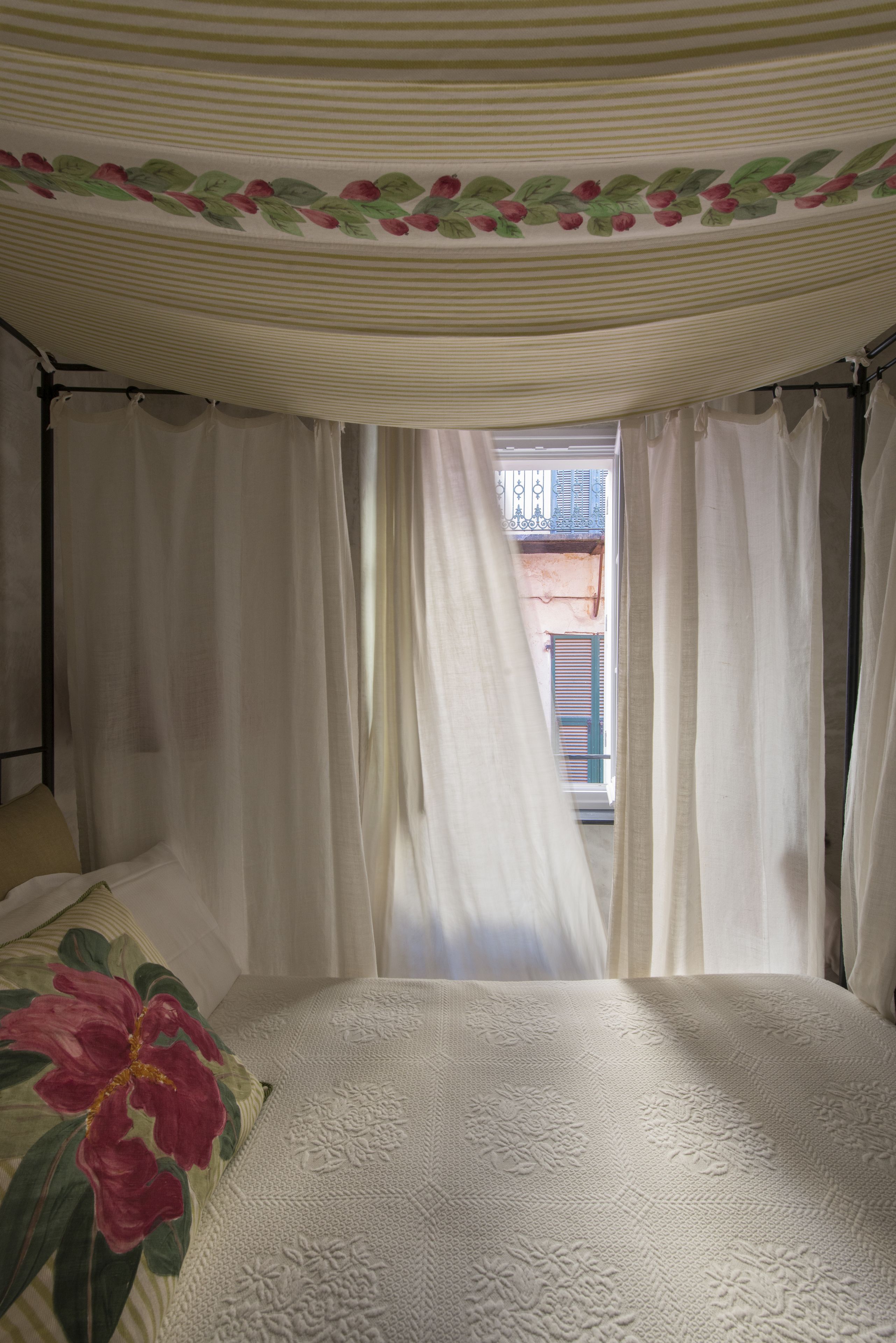 Un dormitorio con cama con dosel, cortinas blancas y vistas al balcón exterior.