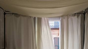 Un dormitorio con cama con dosel, cortinas blancas y vistas al balcón exterior.