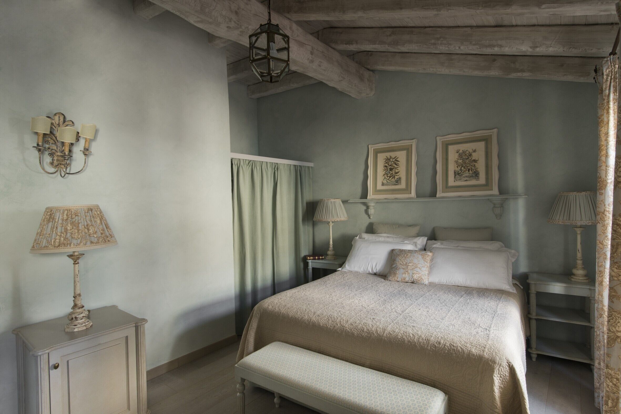 A bedroom with a large bed, a bench, a nightstand with a lamp, and two wall-mounted lamps.
