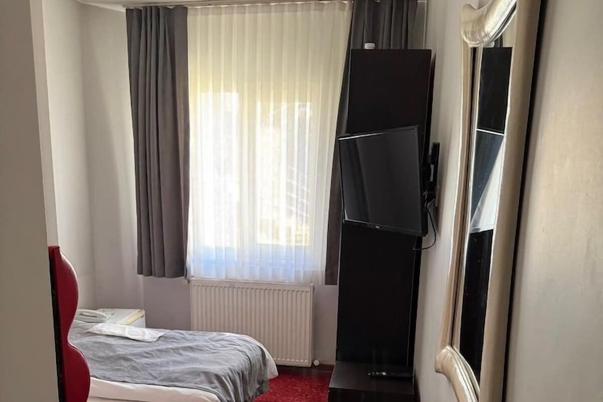 A hotel room with two beds, a red carpet, a television on a stand, and a window with curtains.