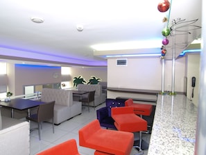 Eine moderne Hotelhalle mit Sitzgelegenheit, einer Rezeption und einer Zierpflanze.