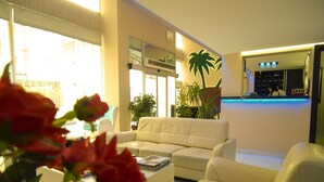 A modern living room with a white leather sofa, a coffee table with magazines, and a large potted plant. - Timya Hotel (Istanbul)
