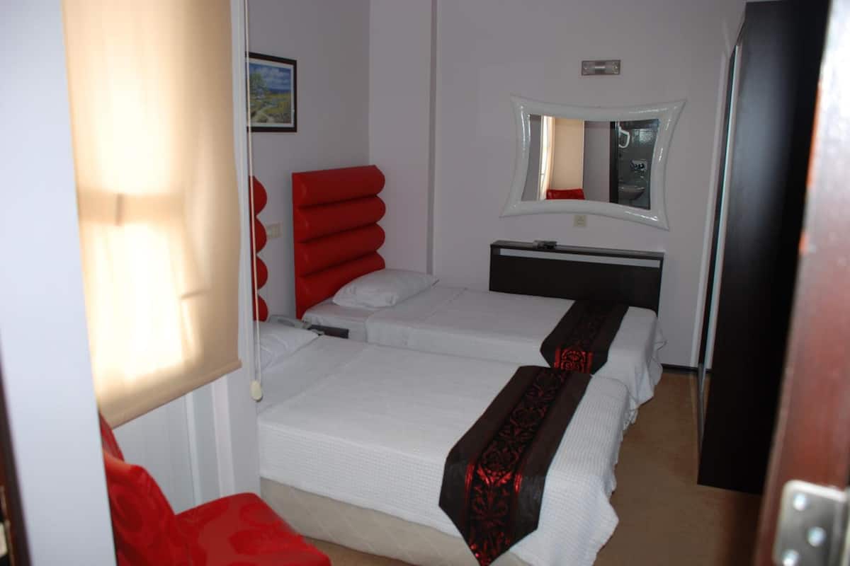 Ein Hotelzimmer mit zwei Betten, einem roten Sessel, einem schwarzen Kopfteil, einem weißen Nachttisch und einem Spiegel an der Wand.