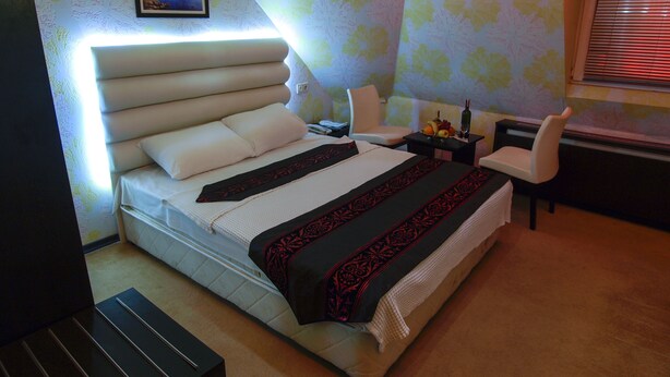 A bedroom with a large bed, a bedside table with a lamp, a chair, and a window with blinds. - Timya Hotel (Istanbul)