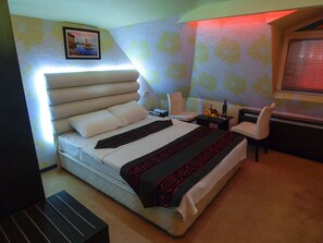 Une chambre à coucher avec un grand lit, une table de chevet avec une lampe, une chaise et une fenêtre avec des stores.