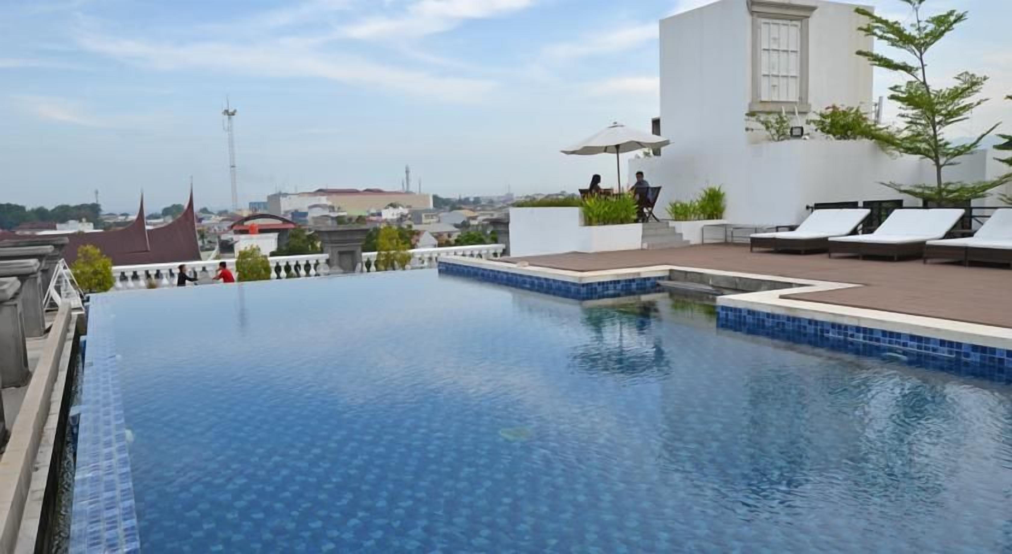 A rooftop infinity pool with lounge chairs and a view of the cityscape.