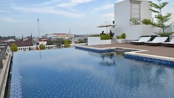 A rooftop infinity pool with lounge chairs and a view of the cityscape.