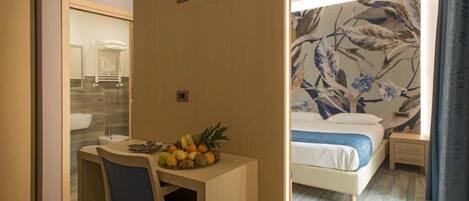 Habitación de hotel con cama, escritorio con fruta, espejo y baño con lavamanos y toallero.