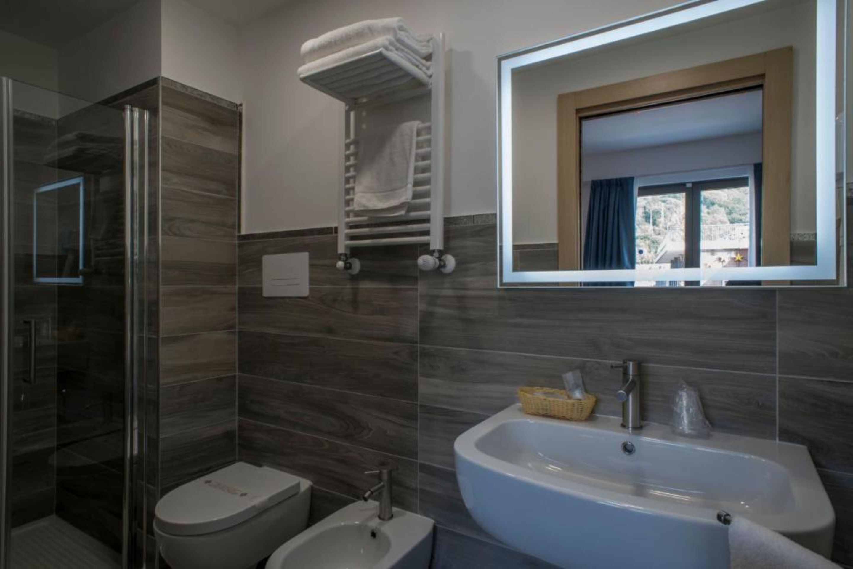 Une salle de bain moderne dotée d’une douche à parois de verre, de toilettes, d’un bidet, d’un grand lavabo et d’un porte-serviettes.