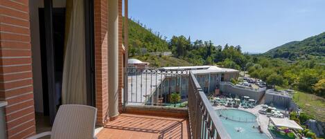 Un balcón con vista a un área de piscina, un restaurante y un paisaje montañoso.