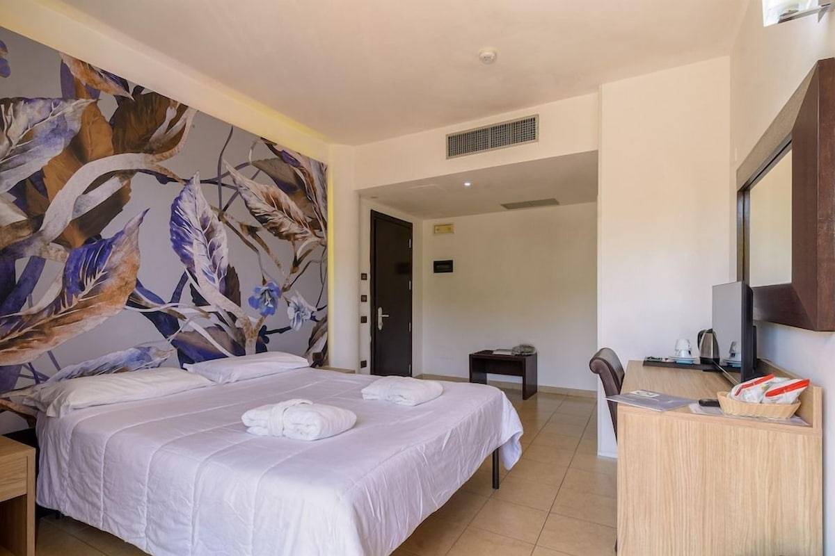 A hotel room with a bed, a desk, a chair, a television, and a door leading to another room.