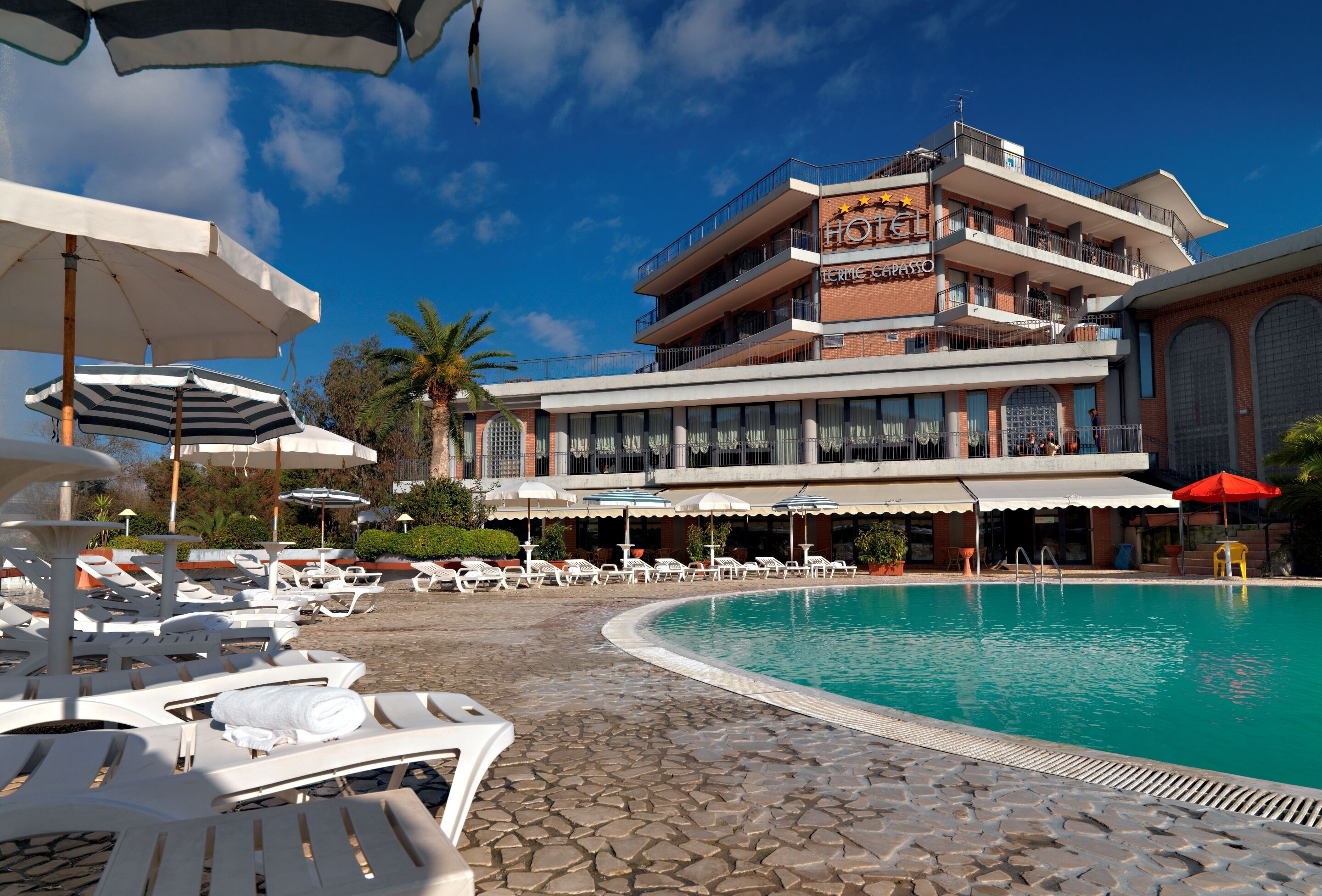 Un hôtel doté d’une piscine, de chaises longues, de parasols et offrant une vue sur un ciel bleu azur.