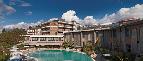 A hotel with a large pool, multiple balconies, and a mountain backdrop.