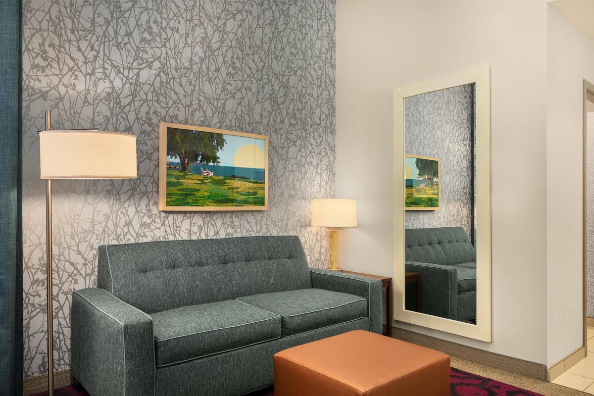 A modern living room with a grey sofa, a small table, a lamp, and a painting on the wall.