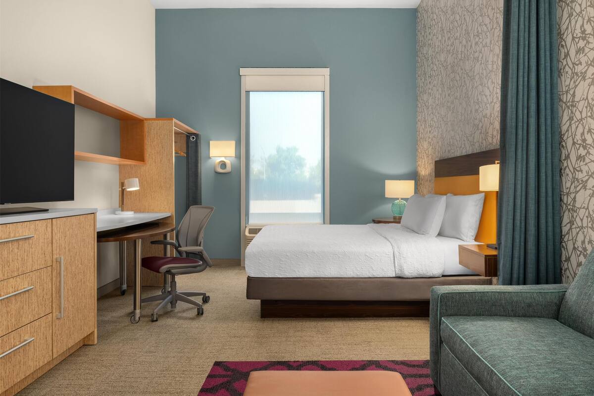 A hotel room with a bed, desk, chair, TV, and a window with curtains.