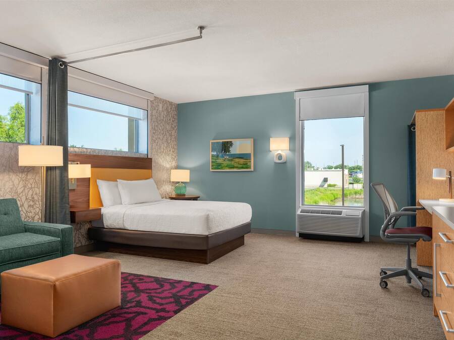 A hotel room with a bed, a desk, a chair, a sofa, and a window with a view of greenery.