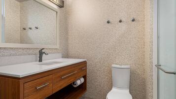 A bathroom with a wooden vanity, a white sink, a toilet, and a shower area.