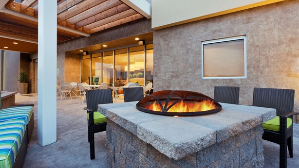 An outdoor patio with a stone fire pit, wicker furniture, and a view of the interior. - Home2 Suites by Hilton Baltimore / Aberdeen, MD (Aberdeen)