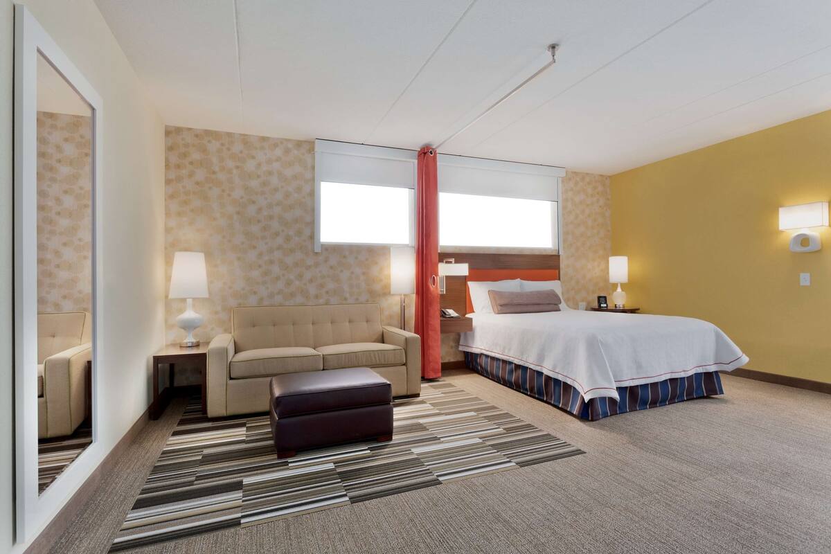 A hotel room with a bed, a sofa, a desk, a mirror, and a window.