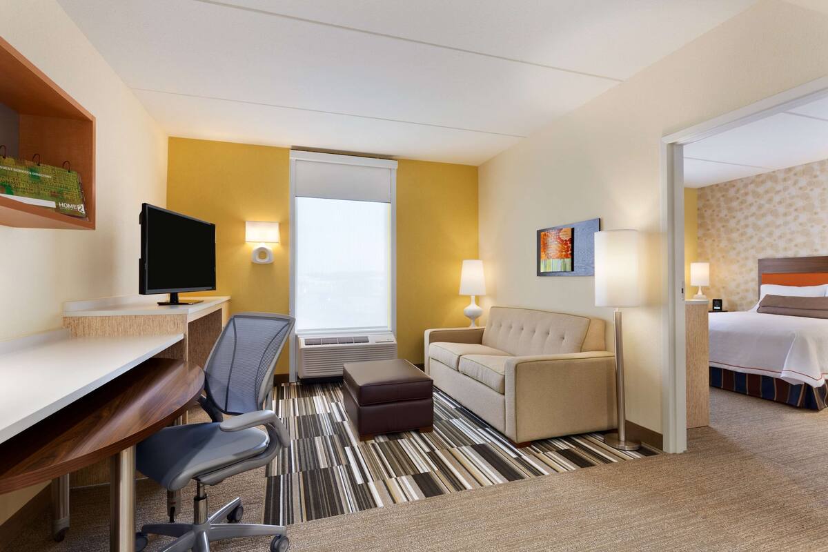 A hotel room with a desk, chair, sofa, ottoman, and a bed.