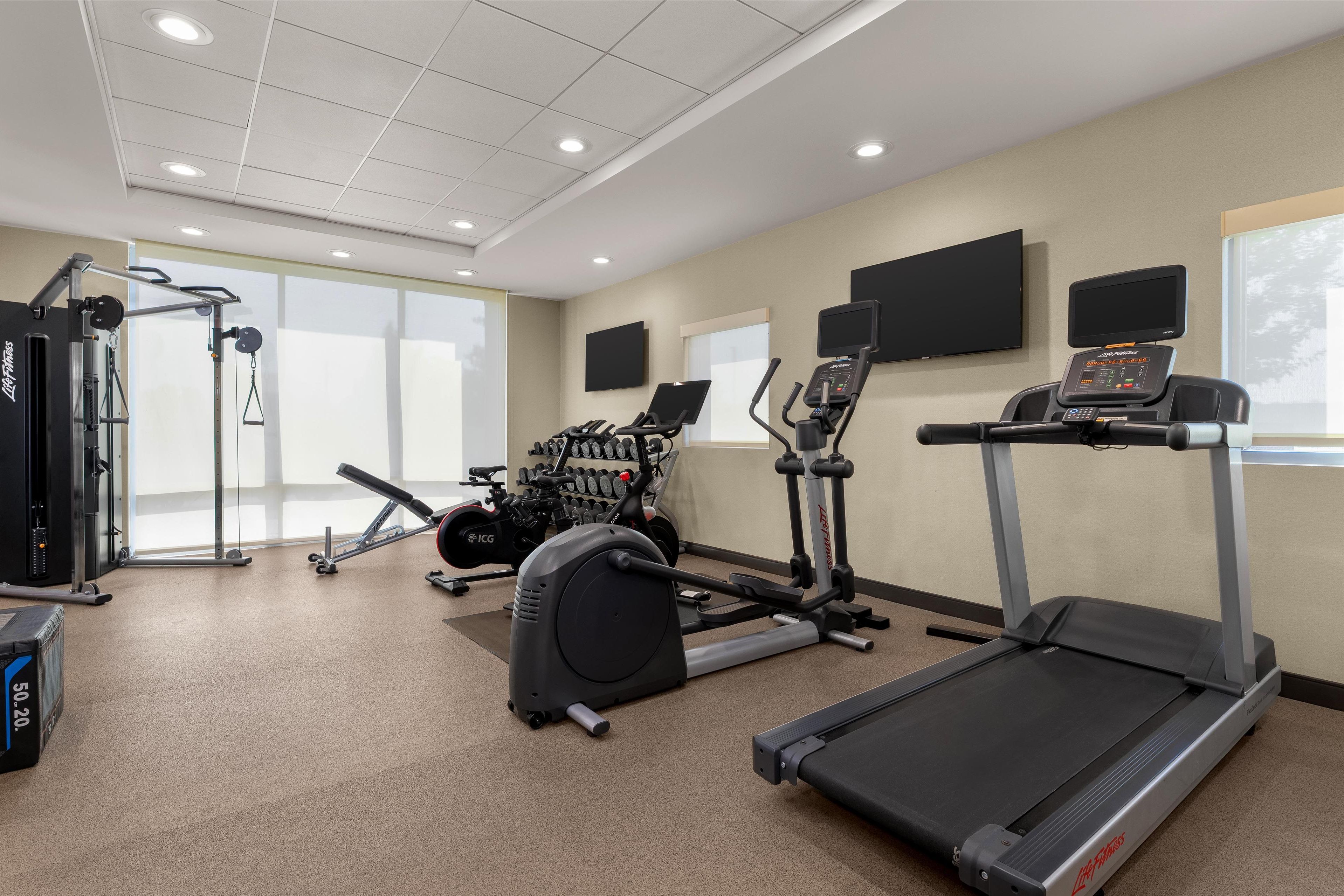 Ein Fitnessraum mit Cardiogeräten, Krafttrainingsgeräten und einem Bildschirm.