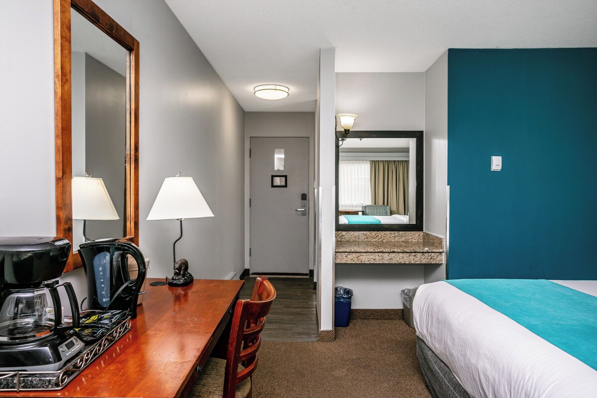 A hotel room with a bed, a desk with a coffee maker, a lamp, and a mirror.