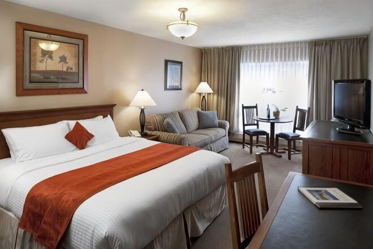 A hotel room with a bed, a sofa, a desk with a TV, and a dining area.