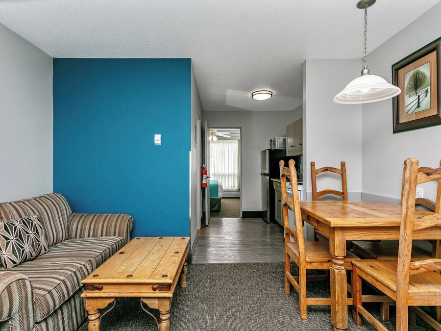 Un espace de vie compact agrémenté d’un mur d’accent bleu, d’un canapé, d’une table à manger en bois et de chaises. On aperçoit une cuisine au fond.