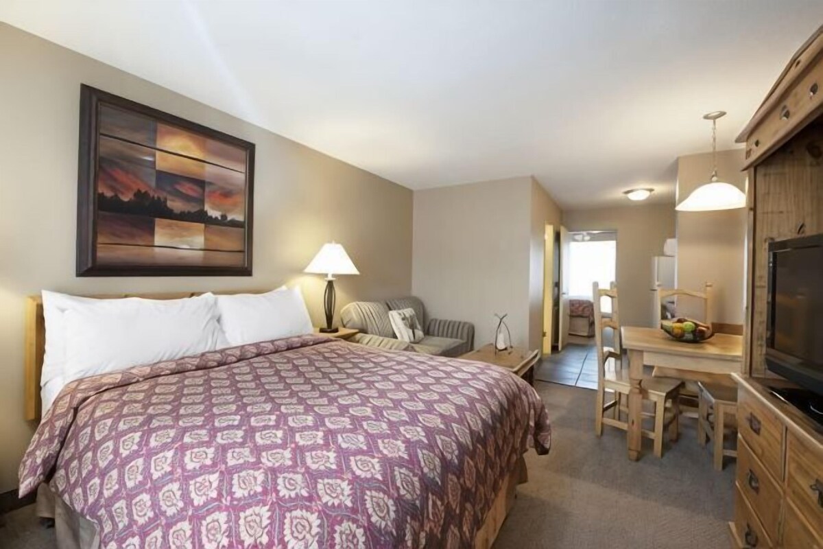 A hotel room with a bed, a desk, a TV, and a dining area.