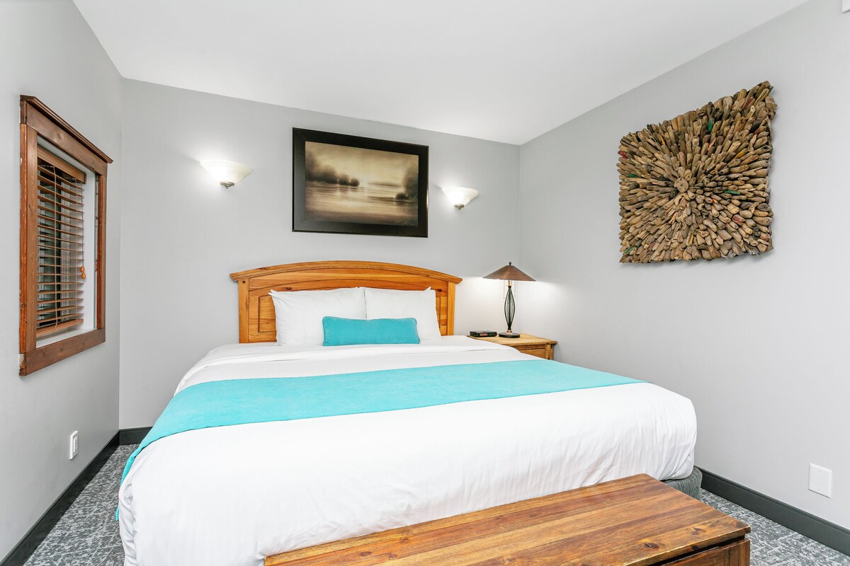 A bedroom with a bed, a nightstand, a lamp, a wall art piece, and a window with blinds.