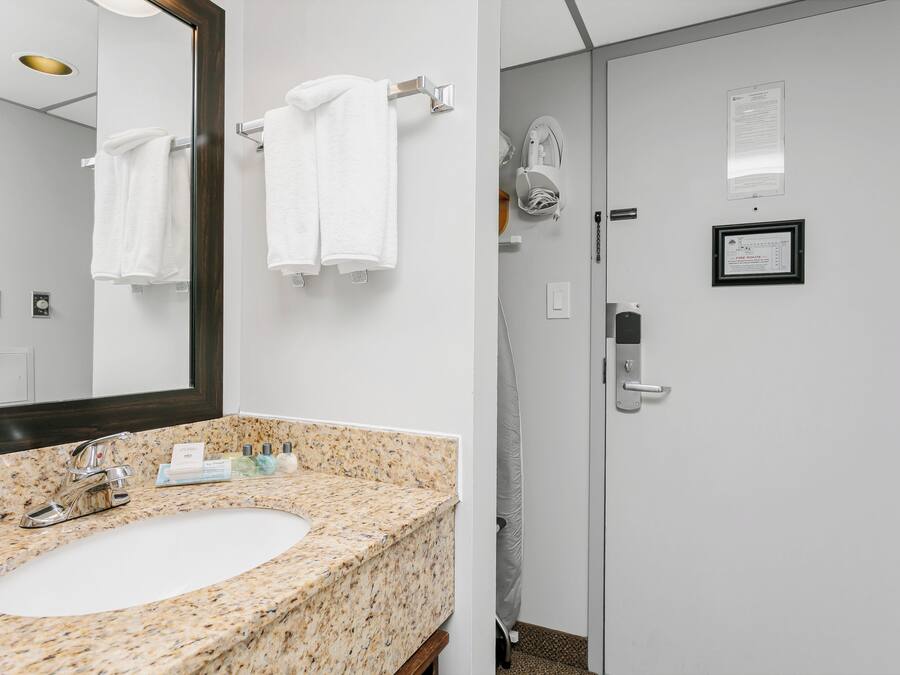 A bathroom with a granite countertop sink, a mirror, and a towel rack.