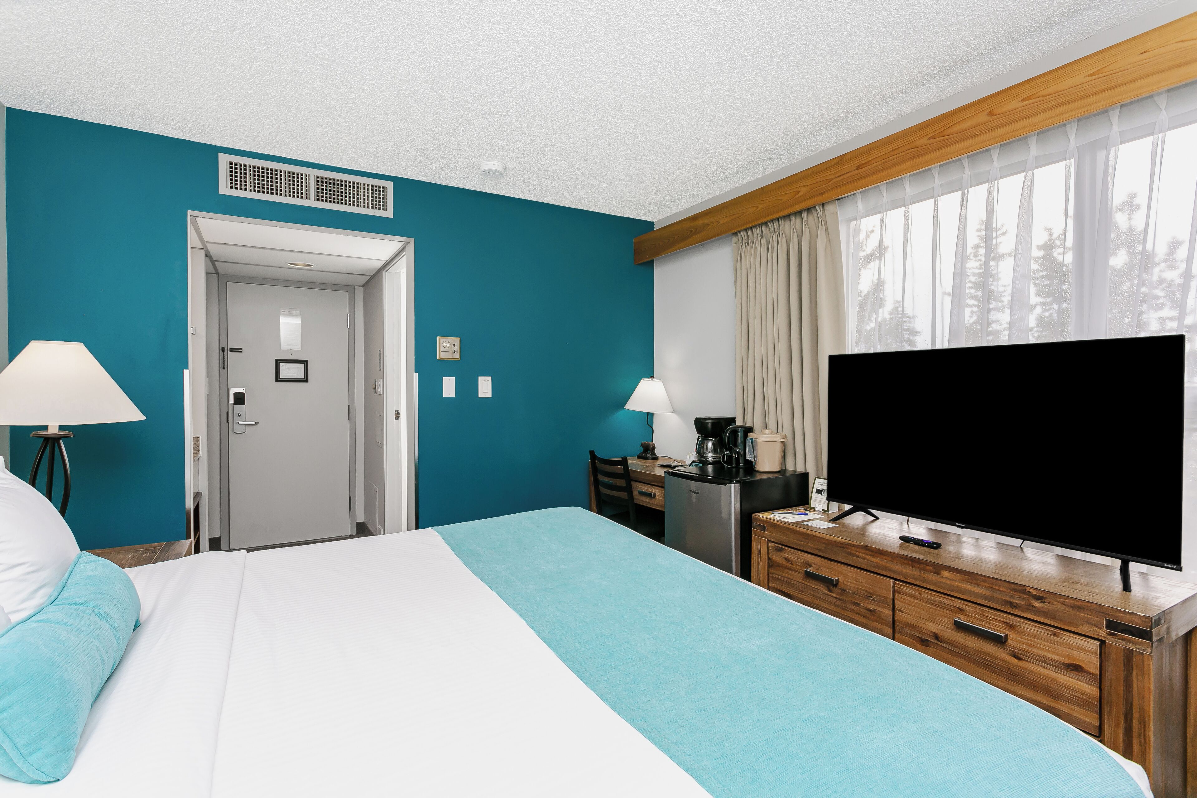 Ein Hotelzimmer mit Bett, Schreibtisch, Fernseher und einem fenster mit Vorhängen.