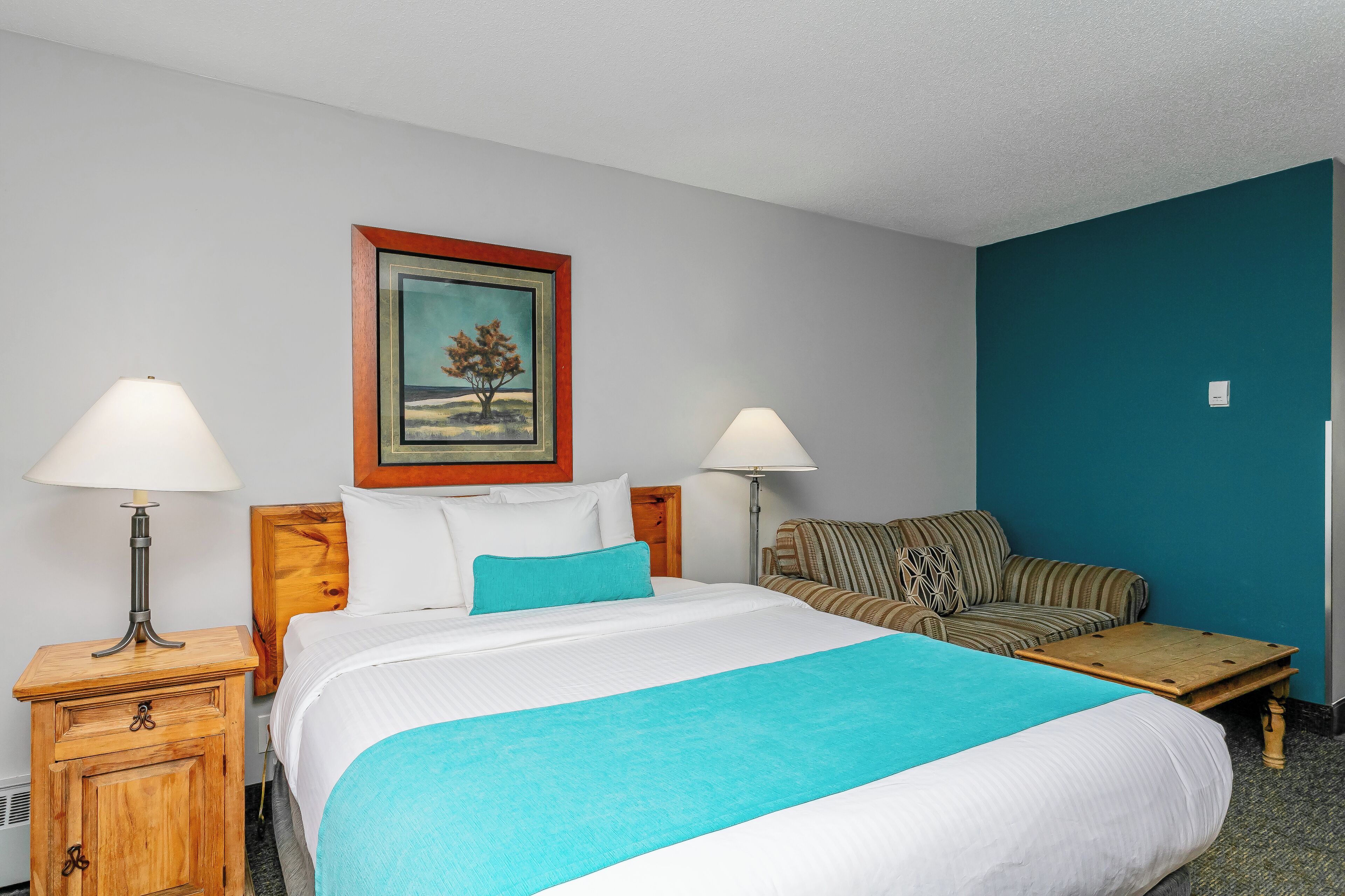 A hotel room with a bed, two nightstands, a lamp, a painting, a sofa, and a coffee table.