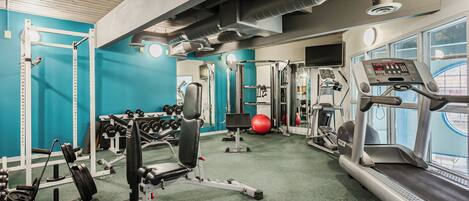 Une salle de sport équipée de matériel d’exercice, d’un tapis de course et d’un ballon rouge.