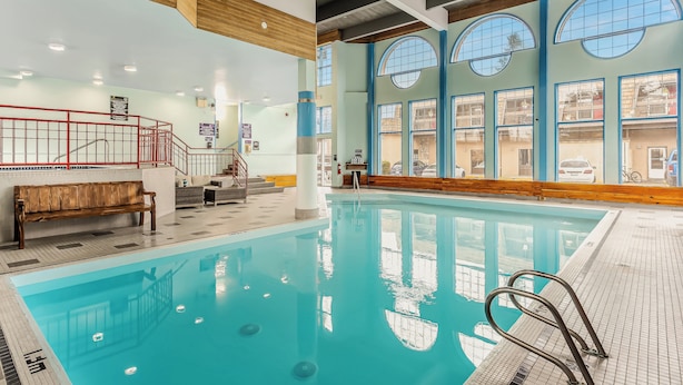 An indoor swimming pool with a wooden bench, a red railing, and large windows with reflections of the outside.