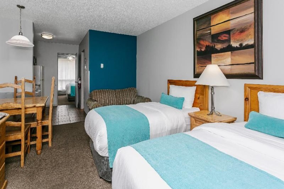 A hotel room with two beds, a dining table, and a painting on the wall.