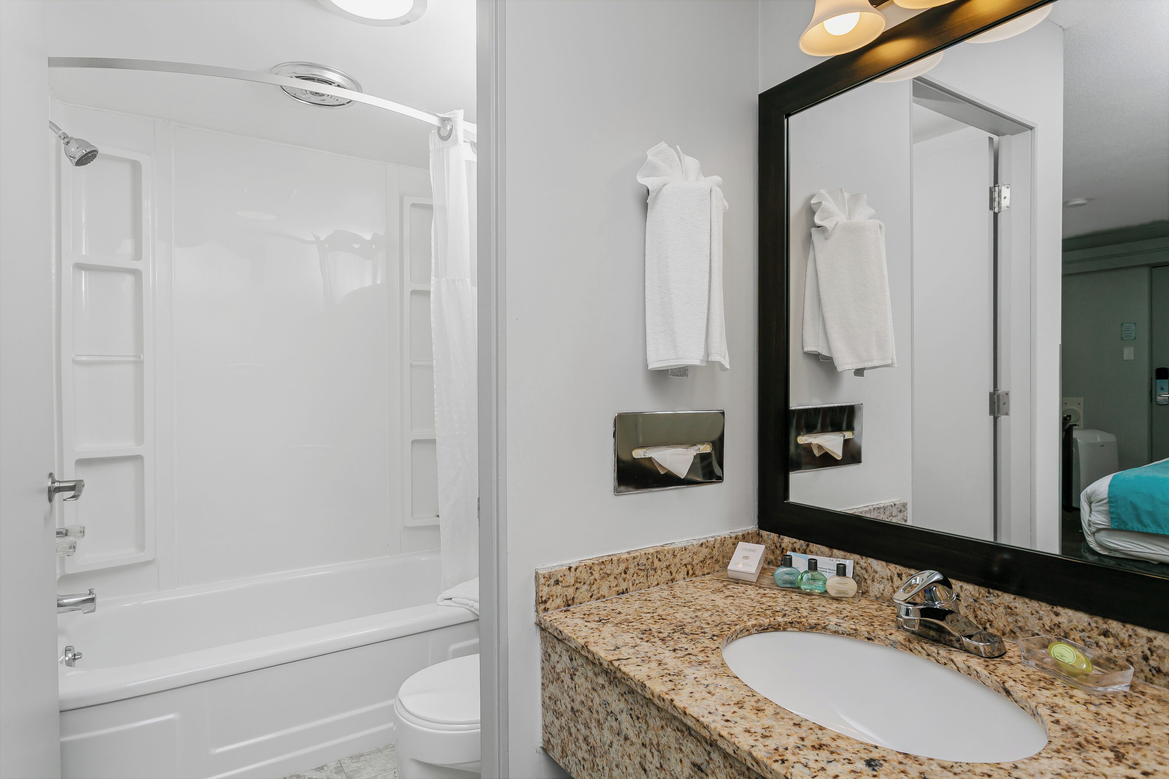Un baño con ducha, inodoro, lavamanos y un espejo grande.