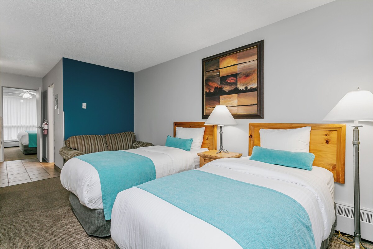 A hotel room with two beds, a painting on the wall, and a floor lamp.