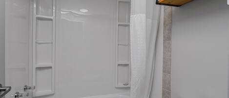 A bathroom with a bathtub, a shower curtain, a towel rack, and a toilet paper holder.