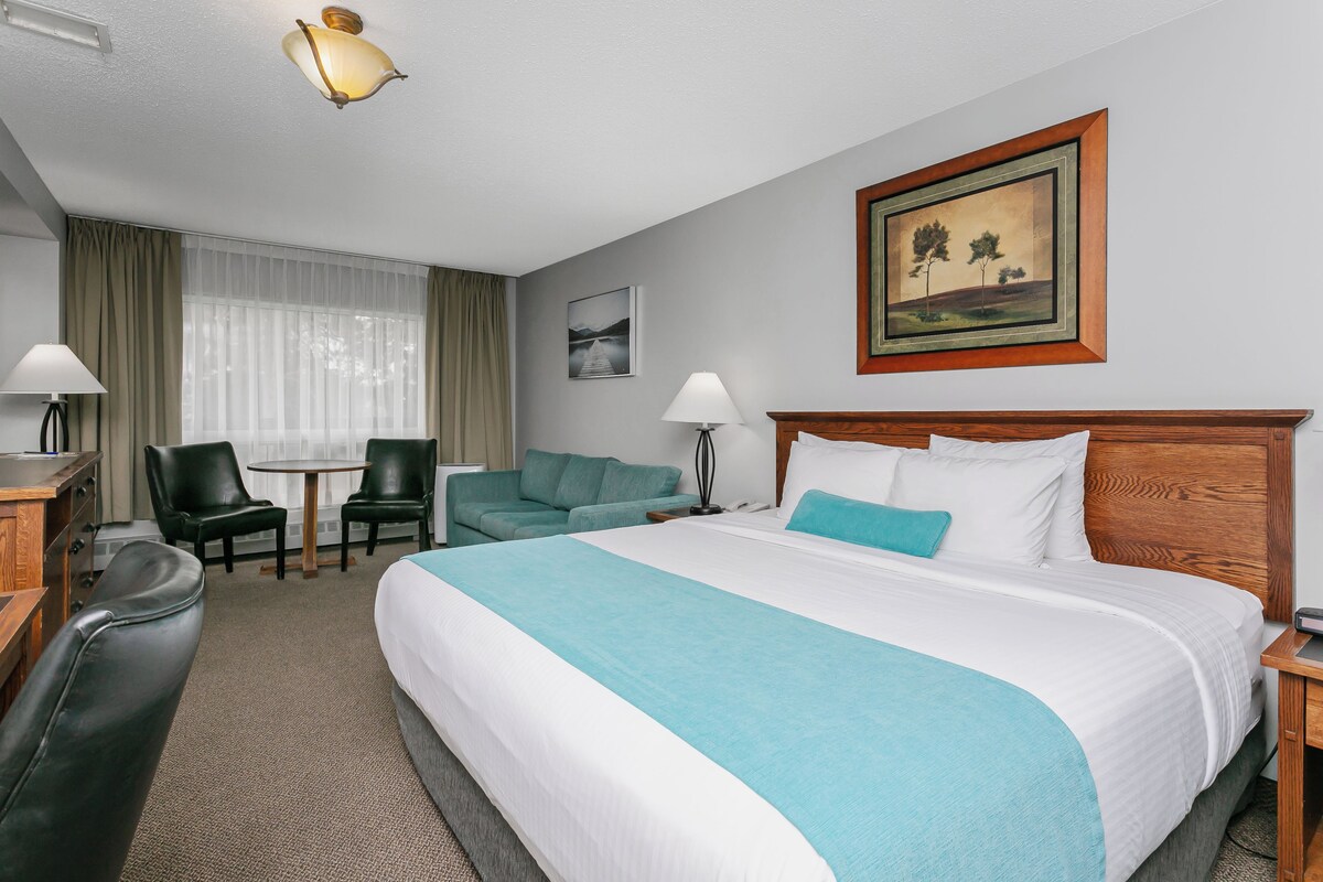 A hotel room with a large bed, a desk, a chair, a sofa, and a painting on the wall.