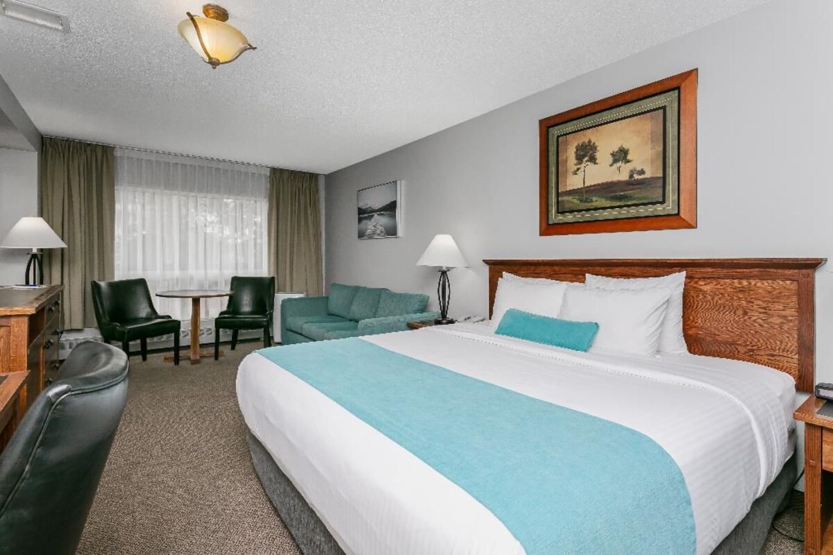 A hotel room with a large bed, a desk, a chair, a small table, and a window with curtains.