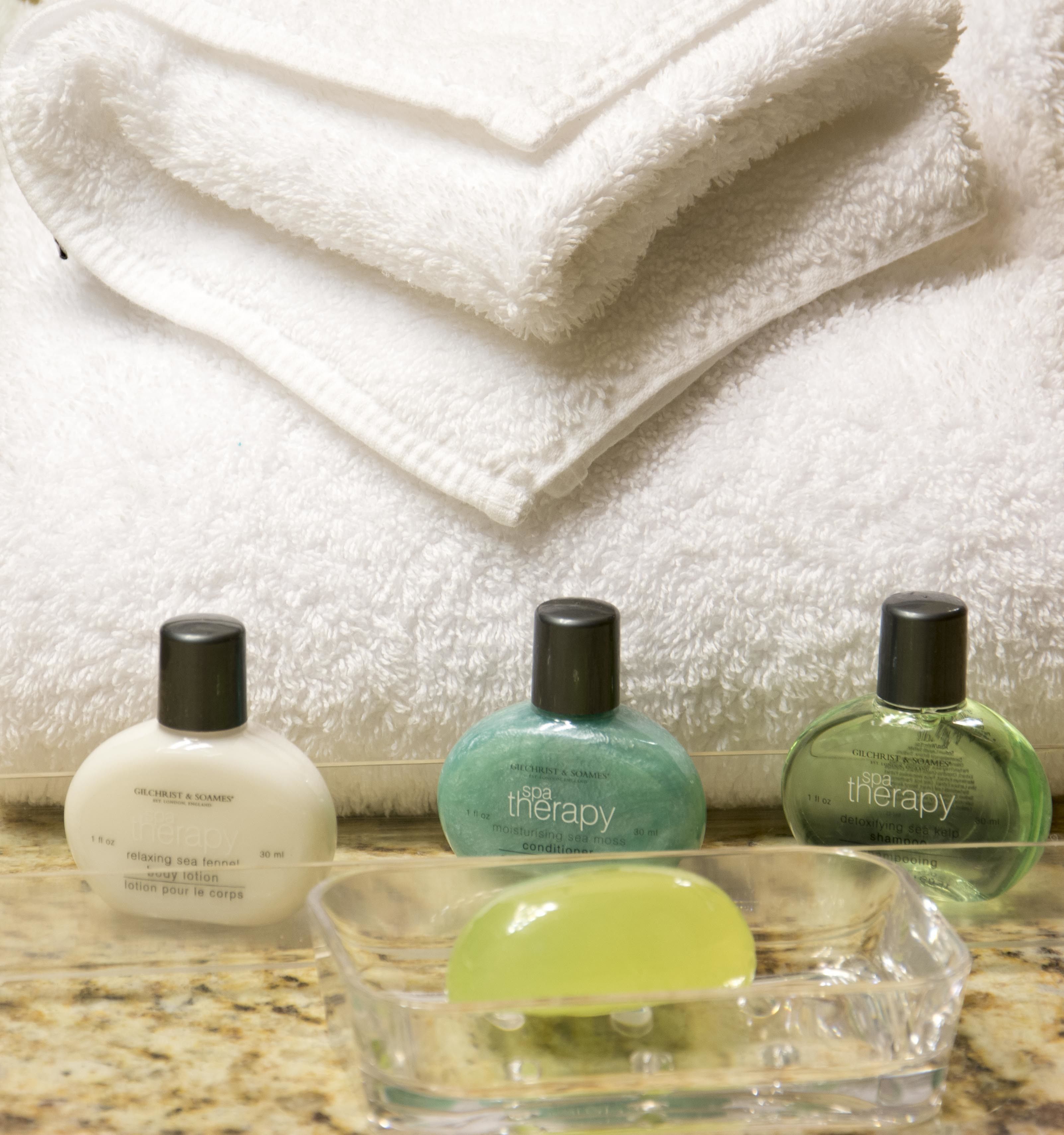 Une salle de bain avec une pile de serviettes blanches, un flacon de lotion pour le corps de la marque Gilchrist & Soames et deux flacons de produits de soins pour le corps.