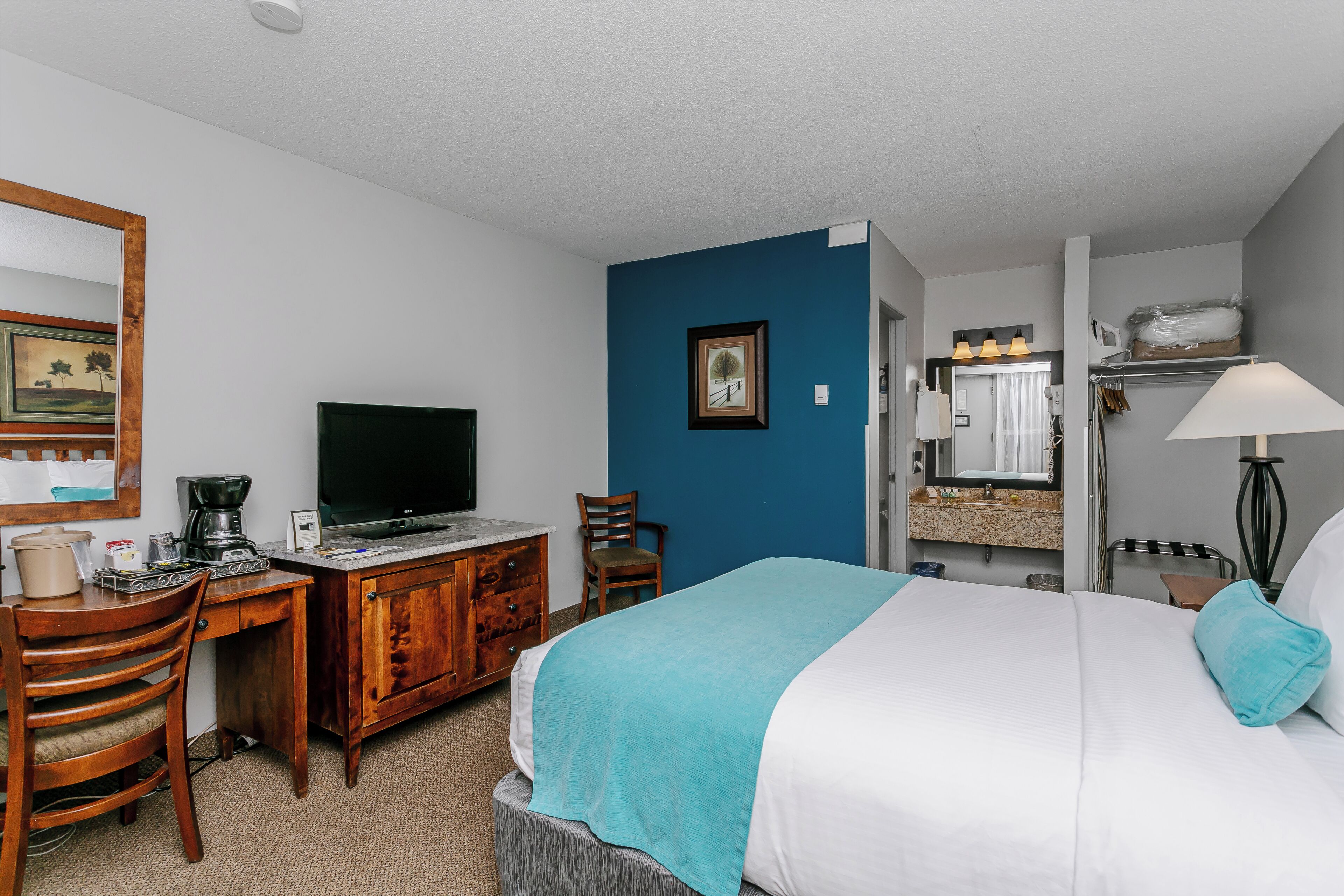 Een hotelkamer met een bed, een bureau met een televisie, een stoel, een dressoir en een badkamer zichtbaar door een geopende deur.