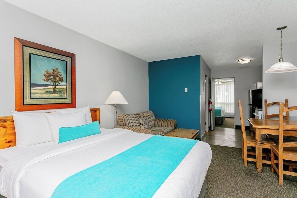 A hotel room with a bed, a sofa, a dining table, and a painting on the wall.
